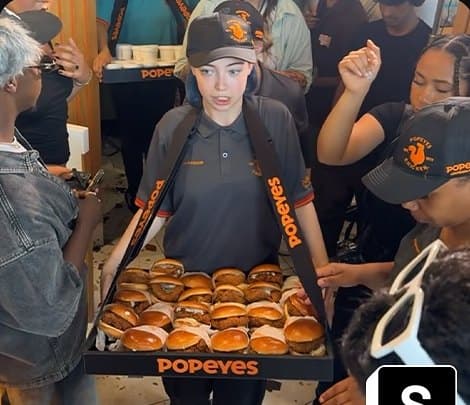 Popeyes staff handing out burgers to a crowd at a live music event