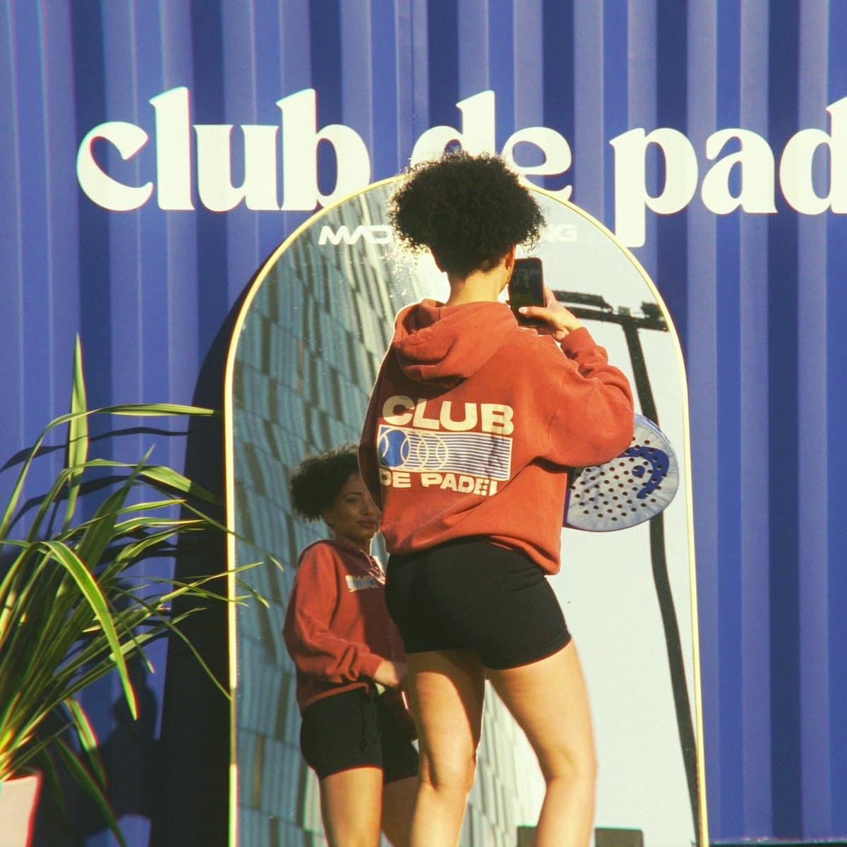 A player photographing her friend against the Club de Padel wall